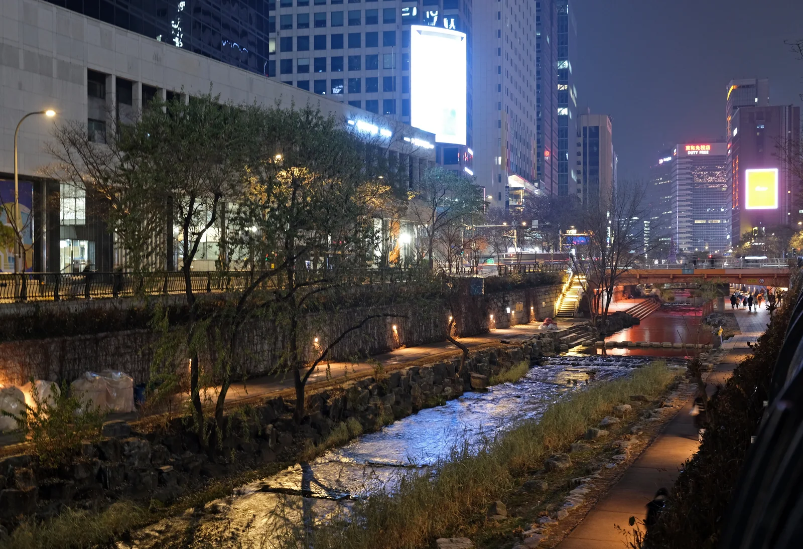 Cheonggyecheon at night with illuminated walking paths, a bridge and city lights reflected in the stream